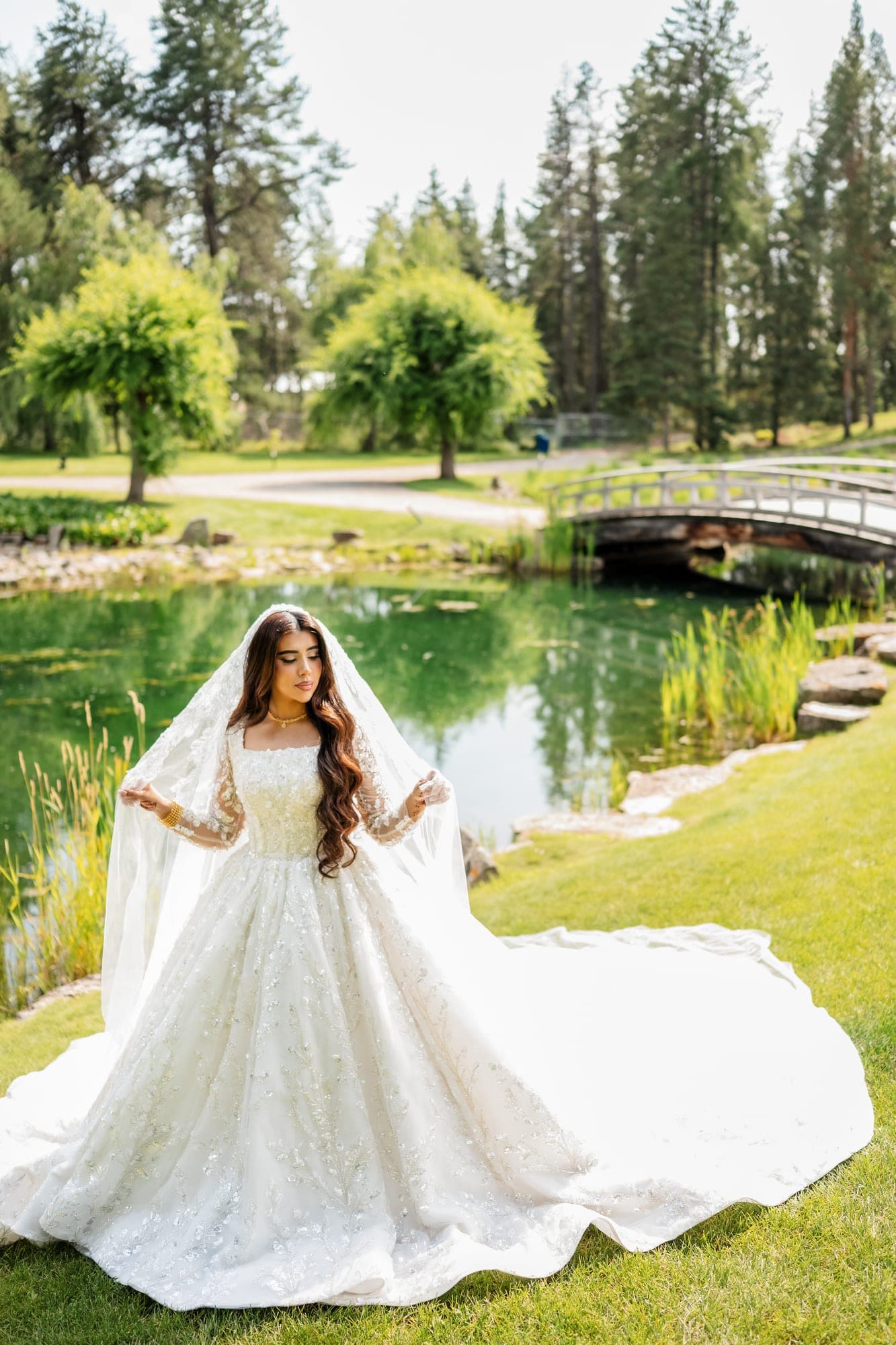A bride arranging her veil beside a garden pond in bright summer light