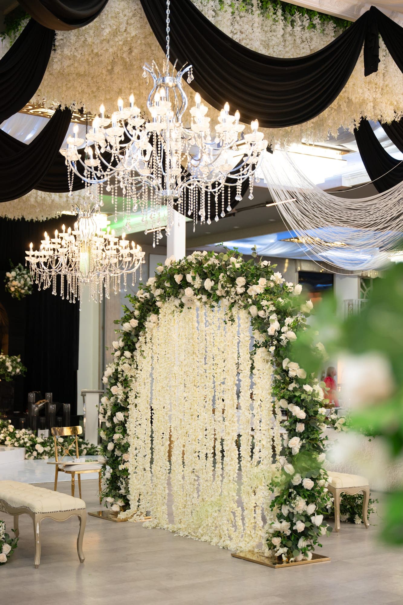 An ivory floral wedding stage beneath crystal chandeliers and black ceiling drapery