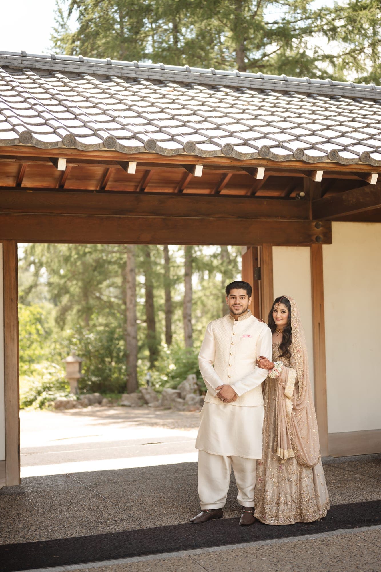 A newlywed couple in ivory wedding attire standing beneath a timber garden gateway