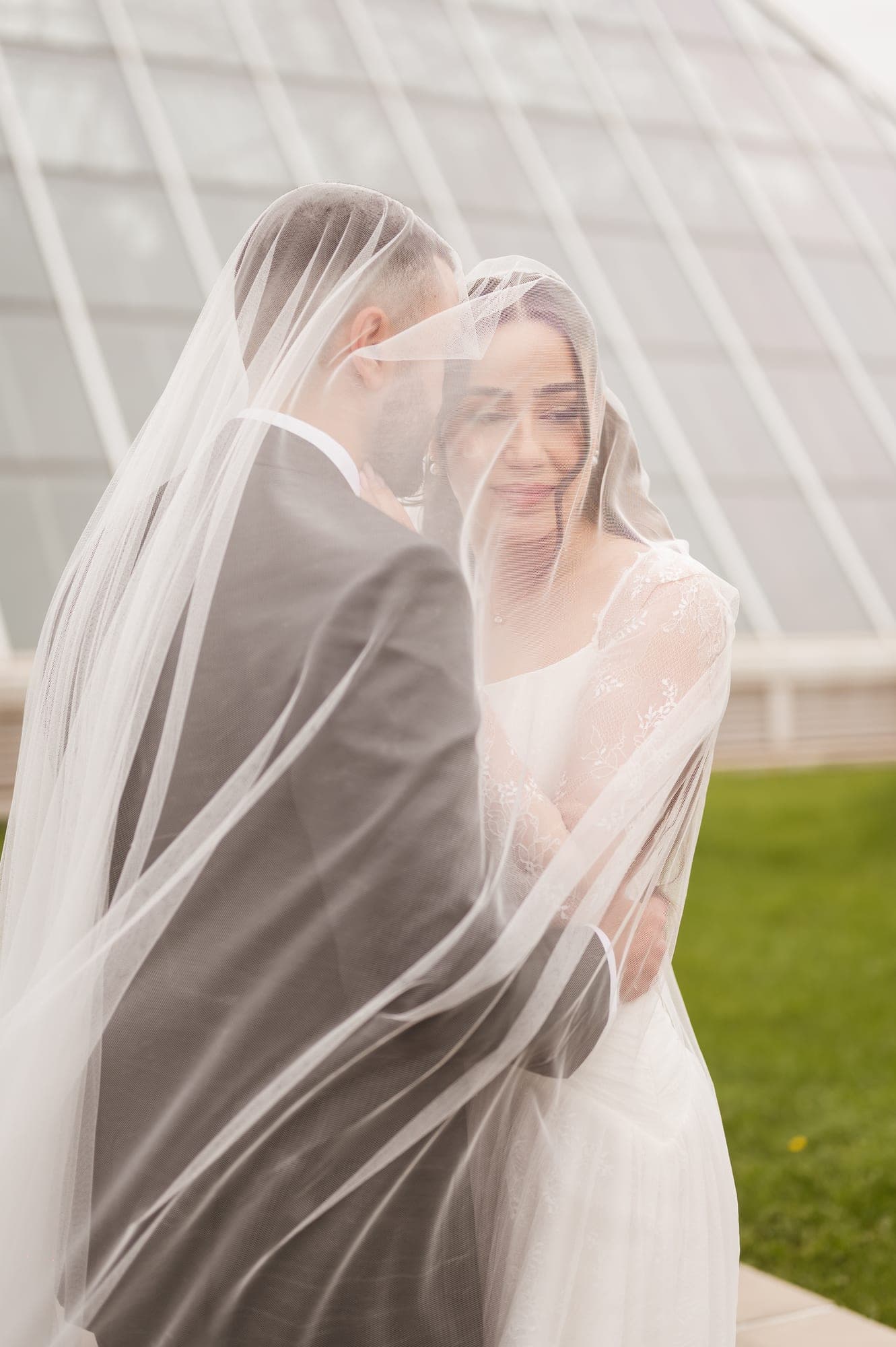 A bride and groom sharing a quiet embrace beneath her translucent veil