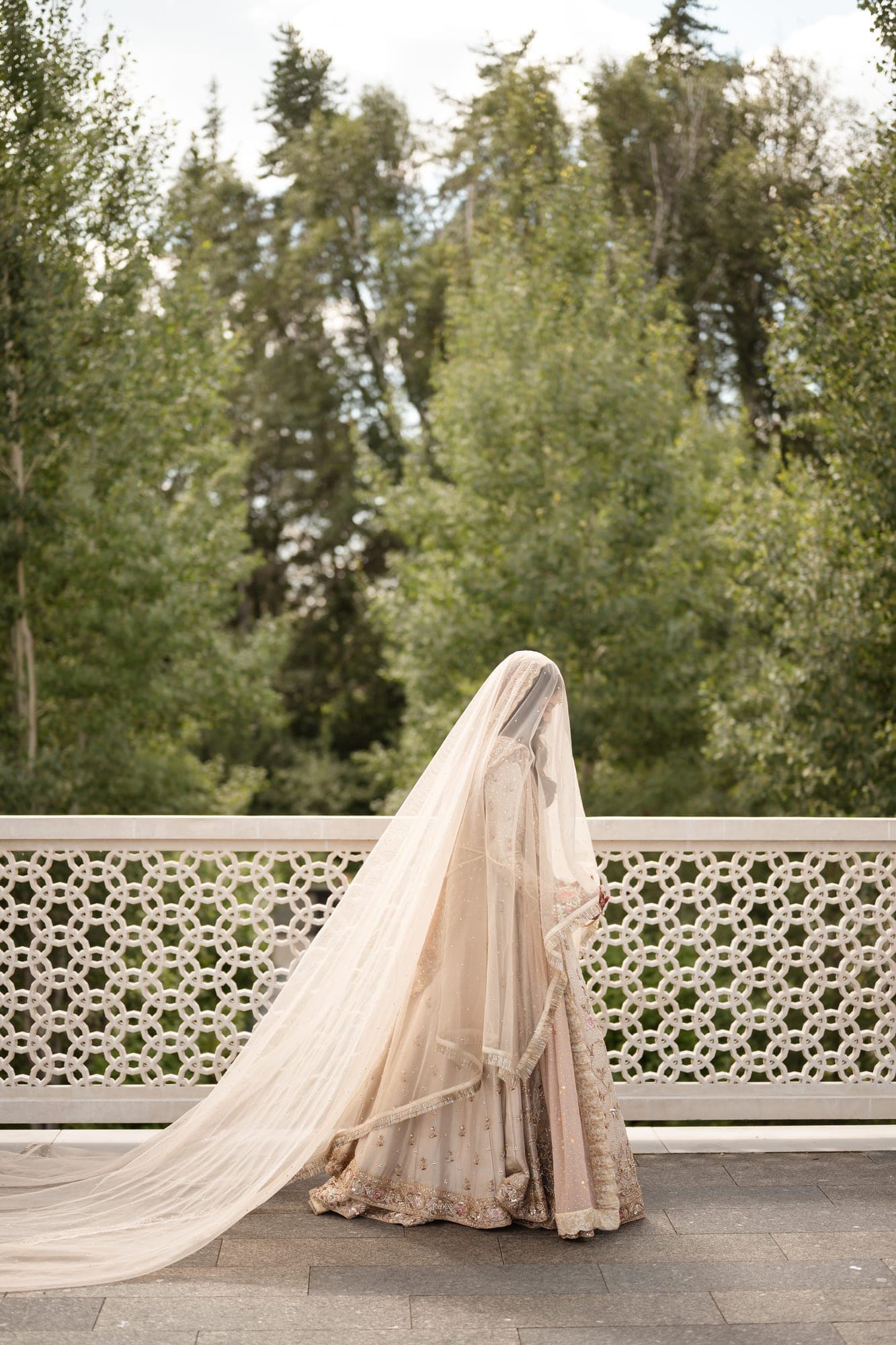 A bride in an embellished ivory gown and long veil walking across a garden terrace